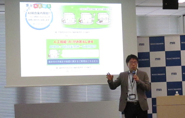 「AIスタッフ総合案内サービス」の機能拡張を説明するMRIの村上文洋上席研究員